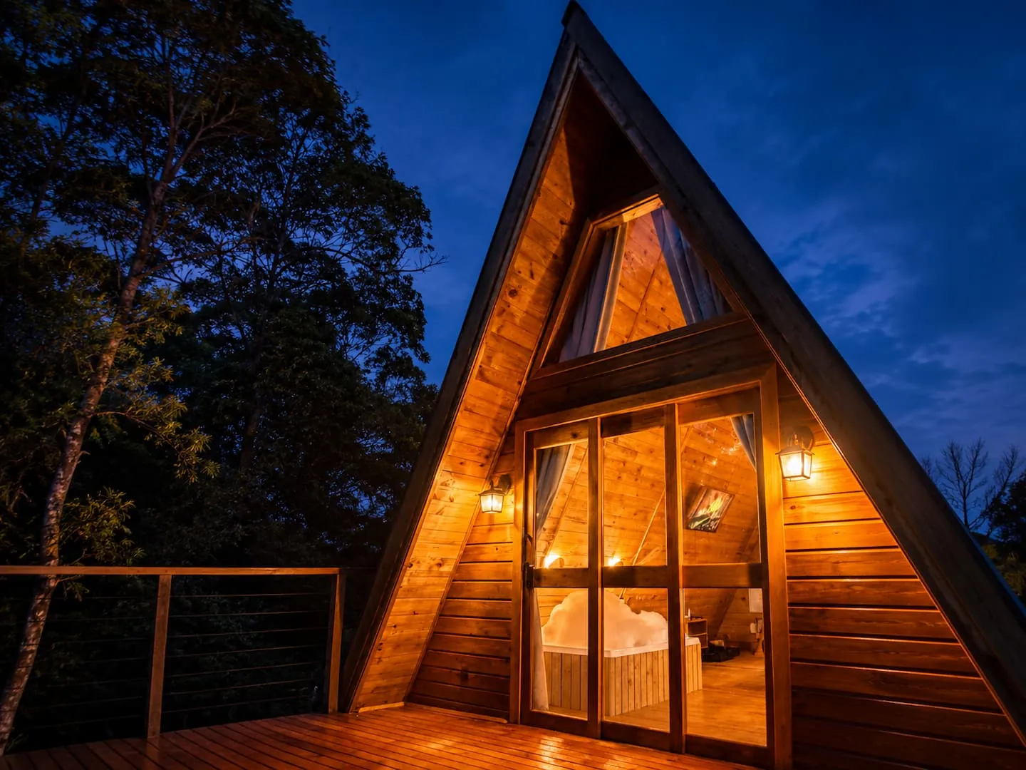 O Chalé Âmbar, chalé em A de madeira, iluminado à noite com as portas abertas para o deck